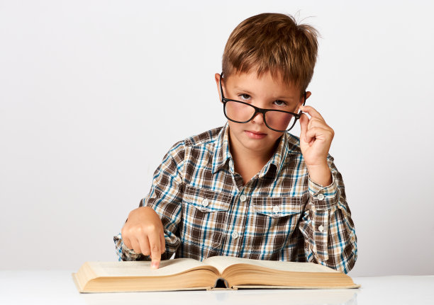 可爱的小男孩拿着书坐在书桌前。七岁的孩子图片下载
