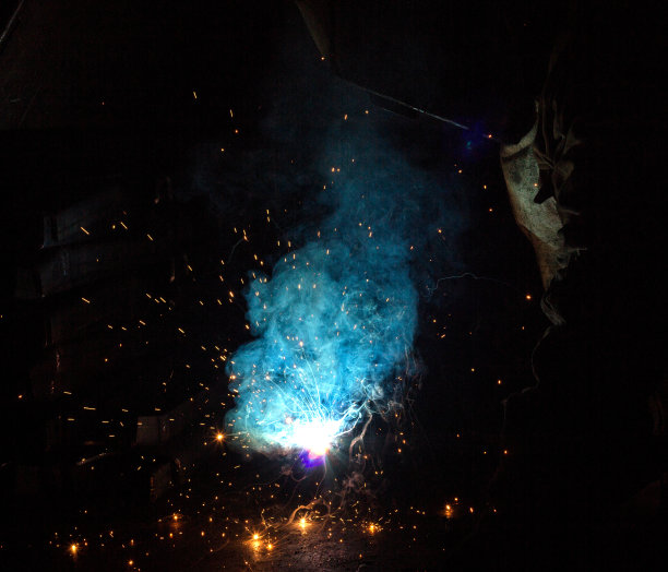 焊工焊接金属零件，有许多火花和油烟，焊接，焊接电弧，闪光，特写，背景图片下载