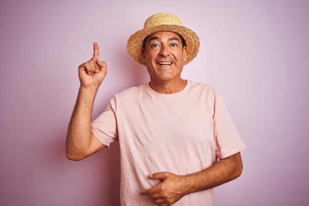 英俊的中年男子戴着夏天的帽子站在孤立的粉红色背景指向手指与成功的想法。退出和快乐。第一。图片下载