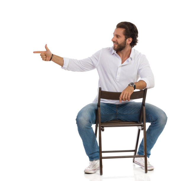 英俊的微笑男子坐在椅子上，看向别处，指着。图片下载