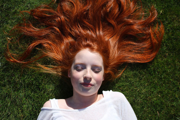 14 / 15岁的红发少女，皮肤苍白，雀斑躺在草地上，眼睛闭着，头发散布在她的头上图片下载