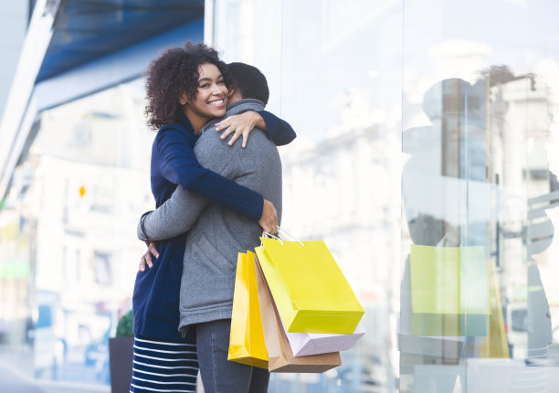 年轻的情侣在购物中心旁边抱着购物袋图片下载