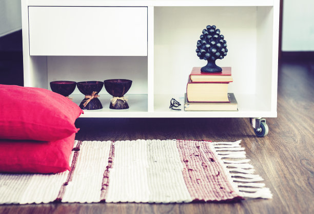 舒适的家庭内部装饰，燃烧的水疗香薰蜡烛椰子壳，金属花瓶，成堆的书，在白色玻璃床头柜附近的多色地毯装饰枕头背景图片下载