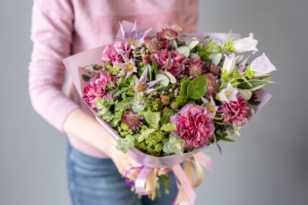 女人手里拿着一束美丽的混合鲜花。花店概念。英俊的新鲜的花束。花交付。绿色和粉红色。素材图片