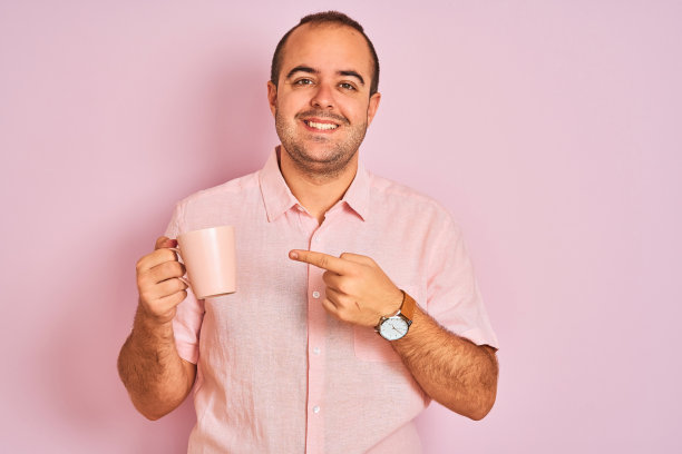 年轻人喝着咖啡，站在孤立的粉红色背景下，很开心的用手和手指指着图片下载