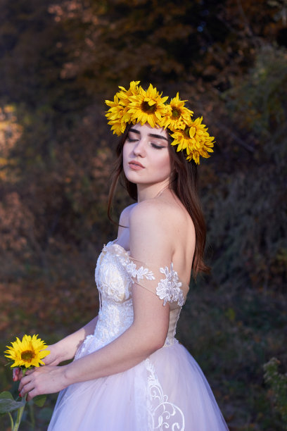 美丽可爱性感的女孩在白色的连衣裙与太阳花花环在她的头享受自然。秋天的时间。图片下载