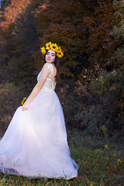 美丽可爱性感的女孩在白色的连衣裙与太阳花花环在她的头享受自然。秋天的时间。图片下载