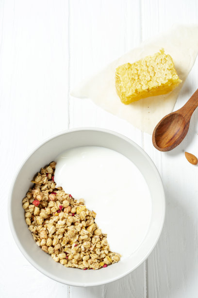 白麦格兰诺拉麦片和低脂酸奶在一个白色的碗，勺子，蜂巢和坚果在白色的木制背景。健康的早餐食品。做早餐。无谷蛋白图片下载