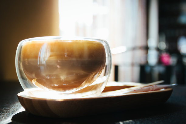 早晨阳光下透明杯子里的卡布奇诺。早上在食堂。阳光。关闭了。咖啡的心情。咖啡店里的光杯。甜而美味的玛奇朵在闪光杯上的桌子。图片下载