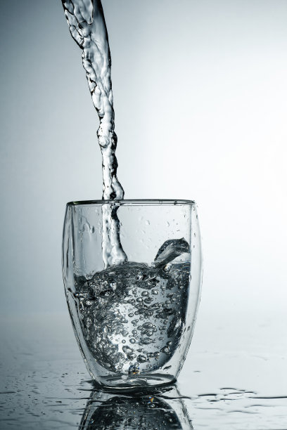 将新鲜、冰冷、纯净的水倒入玻璃杯中。在灰色背景的杯子里装着纯净水。运动冻结溅水晶体水在灰色的背景。图片下载
