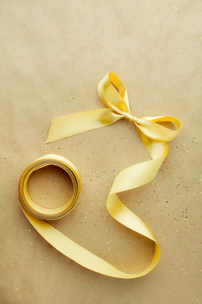 美丽的极简构图与缎面金色蝴蝶结工艺包装纸背景俯视图。介绍准备DIY手工的概念图片下载