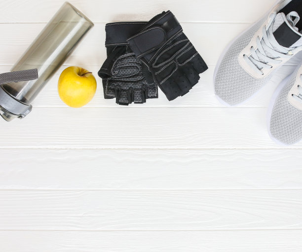 运动的照片。健康的生活方式。装水的瓶子，苹果和皮手套。时尚运动鞋。白色木制背景。完美的平面。图片下载