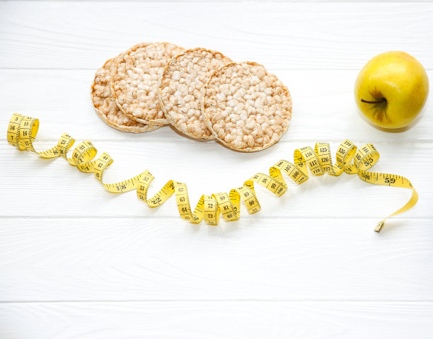 运动的照片。健康的生活方式。健康的概念。低脂脆面包，苹果和一瓶水。适合身体的卷尺。白色木制背景。完美的平面。图片下载