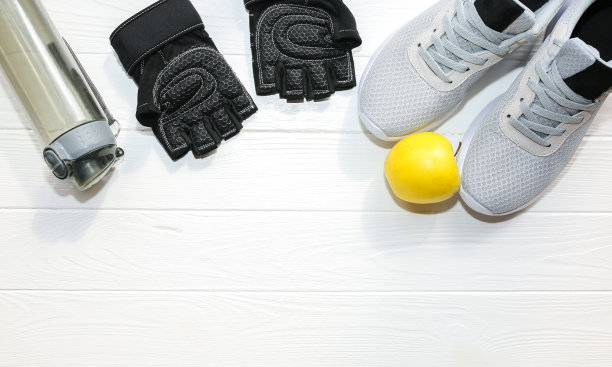 运动的照片。健康的生活方式。装水的瓶子，苹果和皮手套。时尚运动鞋。白色木制背景。完美的平面。图片下载