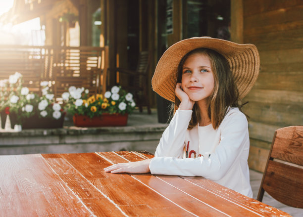 戴着草帽、长着蓝眼睛的迷人少女坐在木屋后院里的餐桌前做梦图片下载