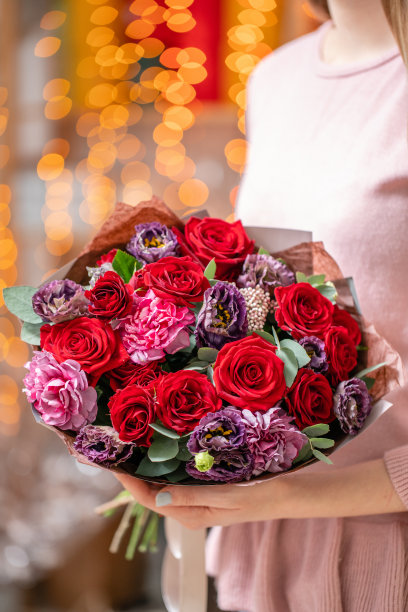 女人手里拿着一束美丽的混合鲜花。花店概念。漂亮的新鲜花束。花交付。背景是花环灯的散景。素材图片