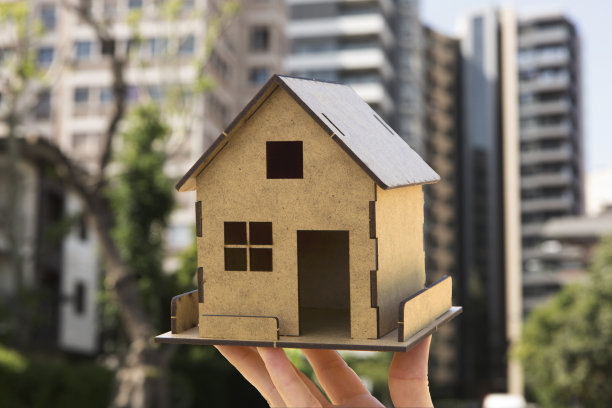 女人的手展示模型房子，公寓大楼的背景。新房，买和租，抵押，房地产概念。水平的细节特写。图片下载