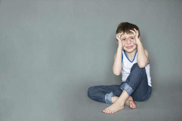 滑稽快乐的男孩把他的手指像眼镜一样放在眼睛附近。快乐的七八岁的孩子。图片下载