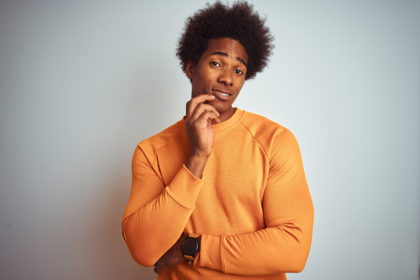 年轻的美国人与非洲式的头发穿橙色毛衣在孤立的白色背景思考看起来疲倦和厌倦抑郁症问题交叉双臂。图片下载
