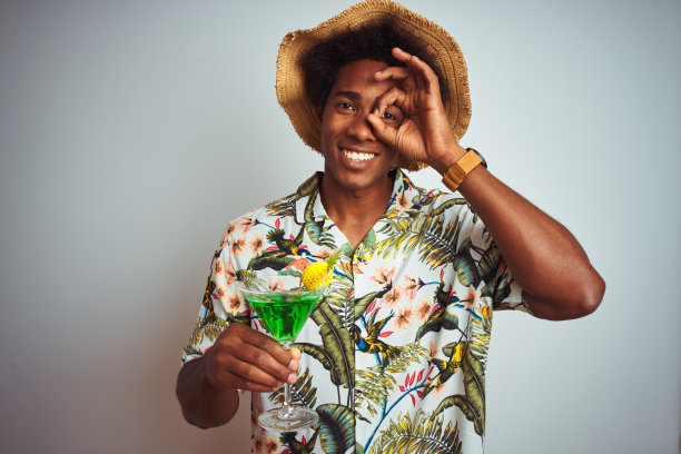 在假日戴着夏天的帽子喝鸡尾酒在孤立的白色背景与快乐的脸微笑做ok手势与手在眼睛透过手指看图片下载