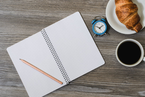 一张桌面的特写，上面有空白的记事本、闹钟、咖啡和甜甜圈。木制背景，俯视图图片下载