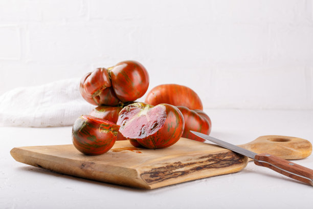 成熟的有机条纹西红柿在白色的背景。传家宝西红柿，木砧板上的黑色斑马。图片下载