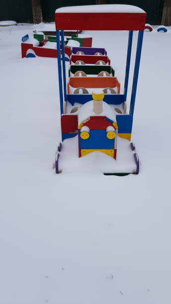 木制火车形状的操场设备，涂上鲜艳的颜色。孩子的火车头在蓬松洁白的雪后。冬季的抽象背景。雪背景与复制空间图片下载