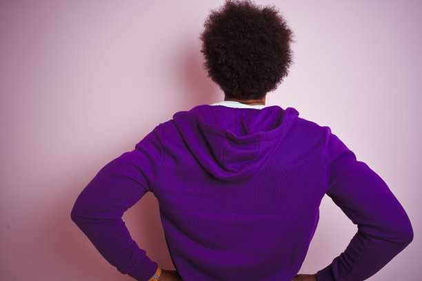 年轻的非洲裔美国人穿着紫色的运动衫站在孤立的粉红色背景站向后看远离手臂在身体上图片下载