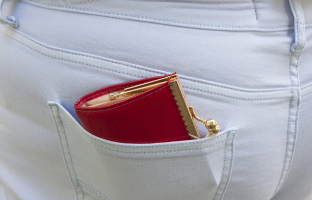 蓝色牛仔裤的口袋里伸出一个镶着金色边的红色钱包。贫穷或财富的概念图片下载