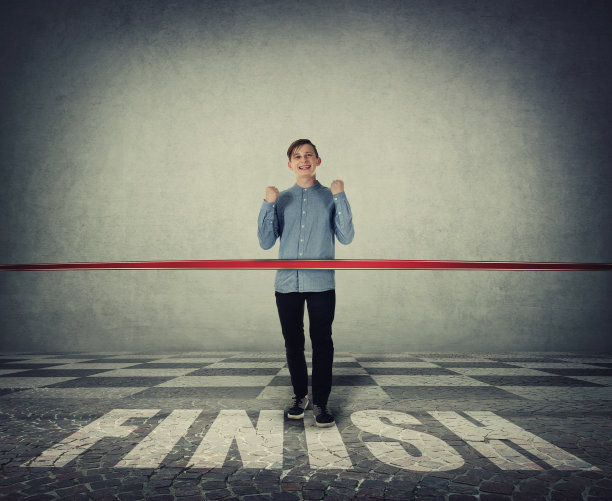 获胜的少年，微笑着庆祝举起拳头。随便一个人冲过终点线，摔断红丝带。挑战必胜、动力与成功理念。图片下载