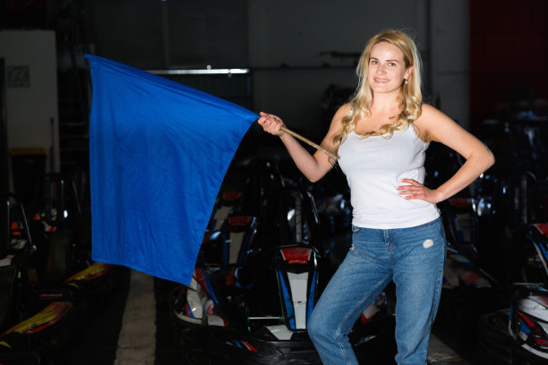 小女孩在卡丁车赛道上举着蓝旗的肖像图片下载