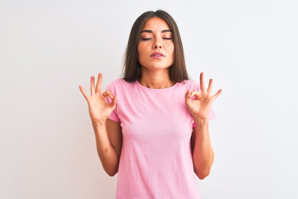 年轻美丽的女人穿着粉红色休闲t恤站在孤立的白色背景放松和微笑，闭上眼睛做冥想手势与手指。瑜伽的概念。图片下载