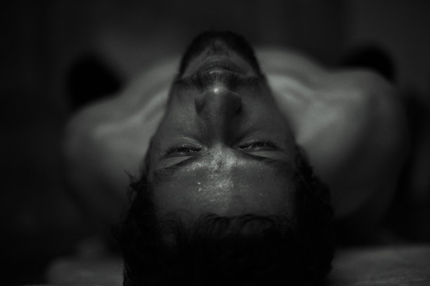 真实的水平特写健康人。强壮的男性在黑暗亲密的气氛中练习瑜伽，躺在地板上体式。胶片颗粒效果。英俊的运动身体在室内捕捉。图片下载