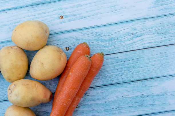 蓝色木桌的背景上放着土豆和胡萝卜。烹饪原料。收成。文本输入的空白图片下载