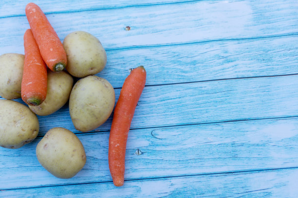 蓝色木桌的背景上放着土豆和胡萝卜。烹饪原料。收成。文本输入的空白图片下载
