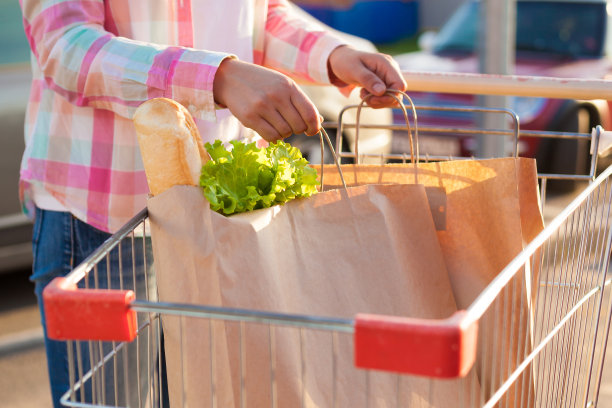 一个年轻的女孩在露天停车场的超市手推车里拿着装着杂货的纸袋。生态购物的概念。图片下载