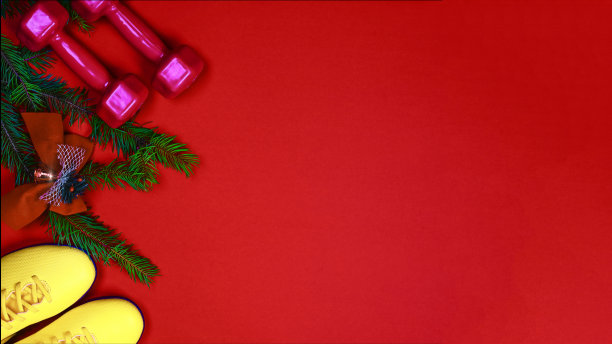黄色的运动鞋，红色的哑铃和红色背景上装饰的圣诞树的树枝。图片下载