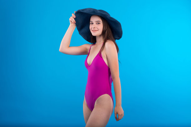 年轻女子在淡紫色泳装内衣和帽子孤立在蓝色背景图片下载