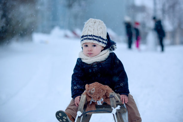 宝宝在雪地里玩泰迪熊，冬天的时候。穿着蓝色外套的小男孩，拿着手提箱和泰迪熊，在冬天的公园里玩耍图片下载