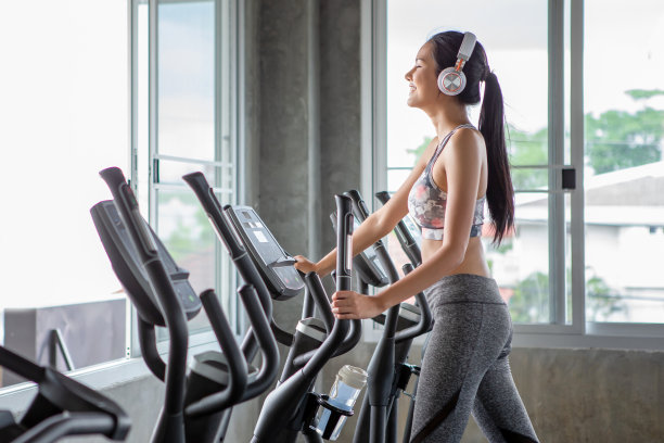 年轻美丽的亚洲女性在椭圆机上锻炼和听音乐耳机在健身馆放松时间。运动女孩锻炼，训练，健康的生活方式图片下载