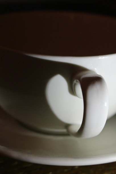 白色的瓷器咖啡杯放在碟上，杯柄的影子投射出一个心形图片下载