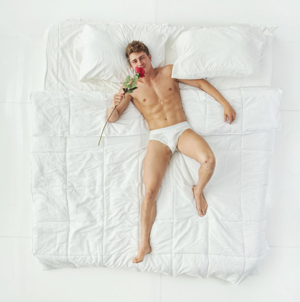 全身/一人/一人/正上方/看着相机/抬头/正面视图20-29岁的成年人英俊的人/苗条的棕色头发/短发白人男性/年轻男子在白色背景的卧室图片下载