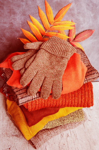 叠起来的暖和的针织女装毛衣，围巾，手套在温暖的颜色和明亮的秋叶。特写镜头图片下载
