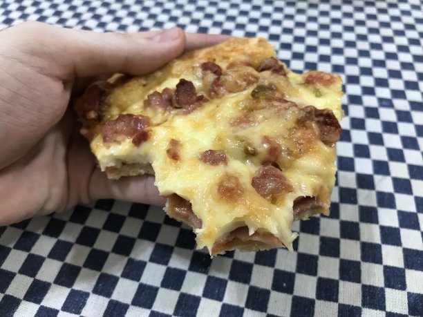 一只手拿着一片吃了一半的火腿和奶酪披萨图片下载