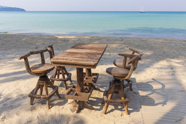 木制的咖啡桌和椅子在热带海滩与蓝色的海洋背景，泰国。节日的概念图片下载