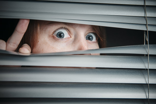 惊慌的女孩，睁大眼睛，透过百叶窗图片下载