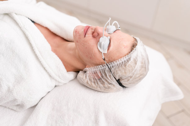 一位年轻女病人的肖像。专业设备抗痤疮光疗。美丽的女人在照片复原程序。美容诊所面部皮肤治疗。图片下载