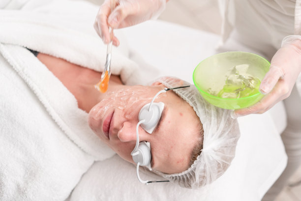 医生给病人涂一种特殊的凝胶。专业设备抗痤疮光疗。美丽的女人在照片复原程序。美容诊所面部皮肤治疗。图片下载