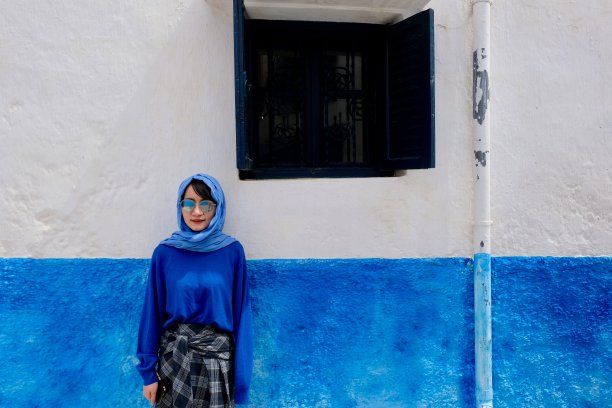 一位穿着蓝色衣服的年轻女子站在摩洛哥阿西拉的蓝白墙前。图片下载