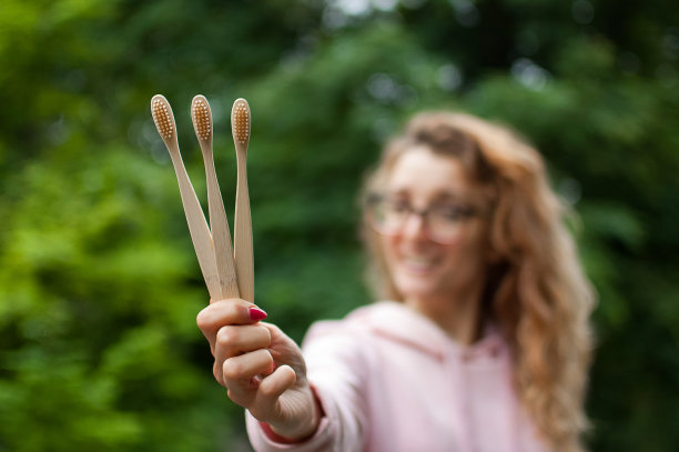 年轻女子面带微笑地在公园外展示木制三竹牙刷，可持续的生活方式，零浪费的理念图片下载